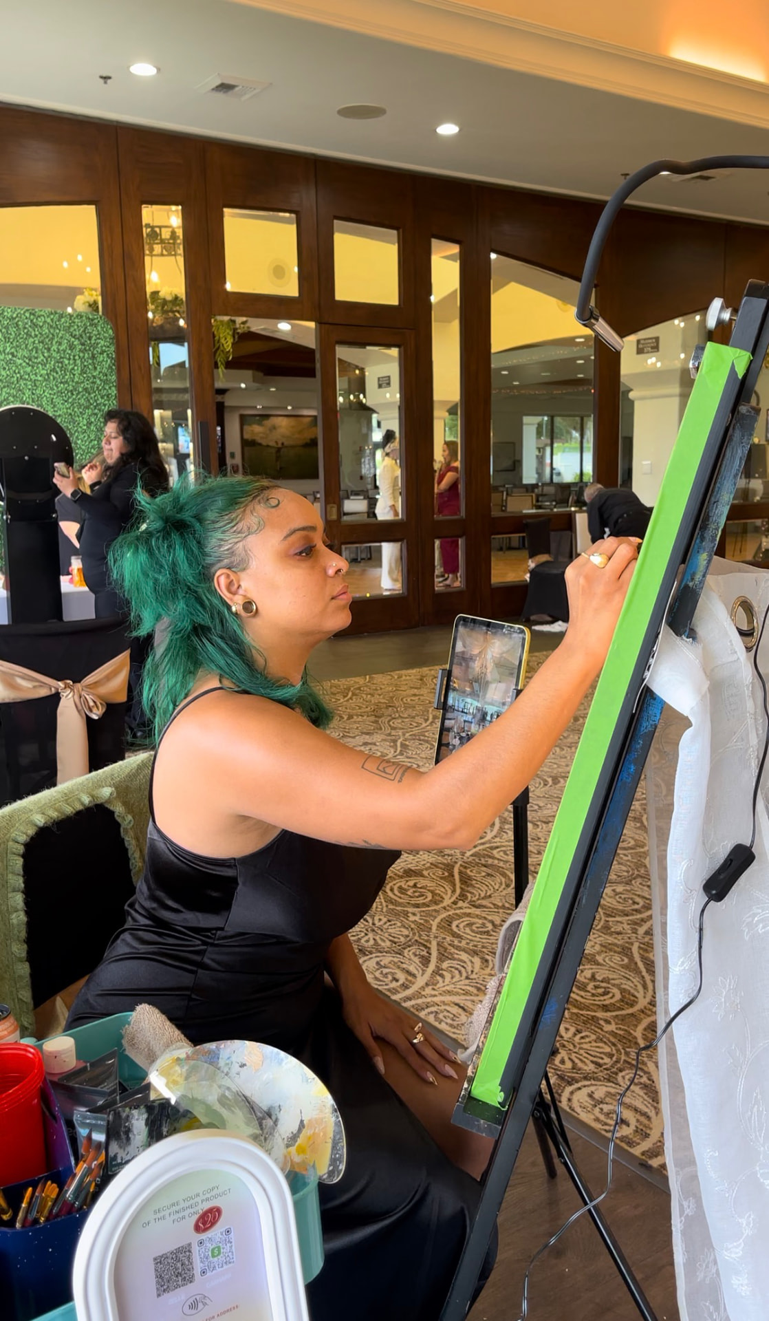Chaleuh in a black dress painting at her easel during a wedding reception