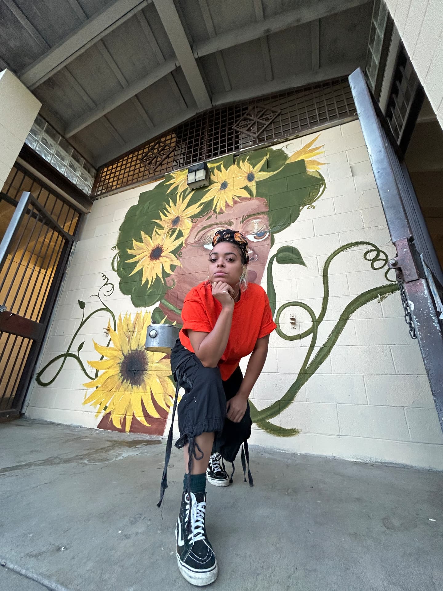 Chaleuh crouching in front of her sunflower portrait mural