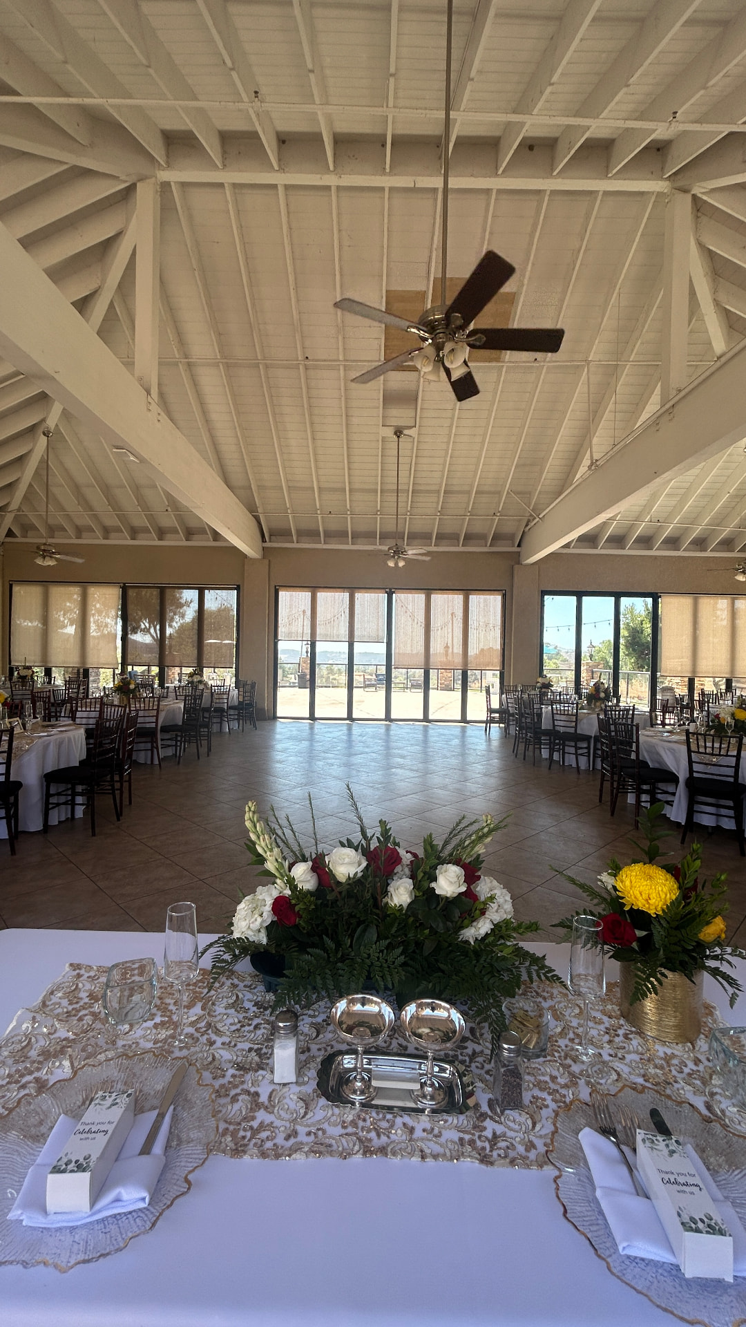 A sunlit hall with vaulted white beams, round tables, and a sweetheart table with red and white roses