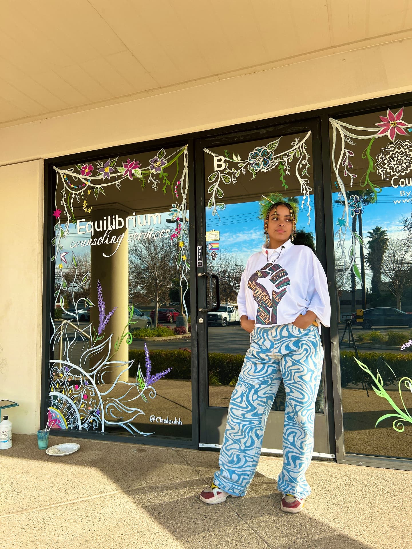 Chaleuh in front of storefront windows hand painted with florals, vines, and lettering
