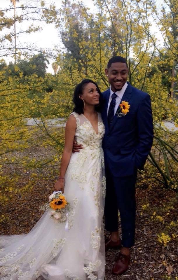 A bride and groom with sunflowers standing beneath a tree of yellow blossoms