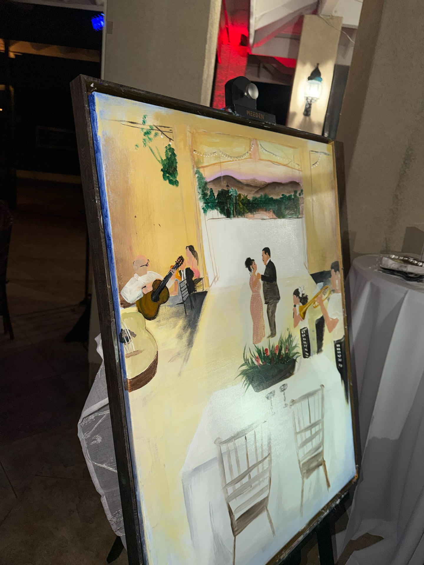 A finished live painting of a couple's anniversary dance with mariachi musicians, on an easel at night