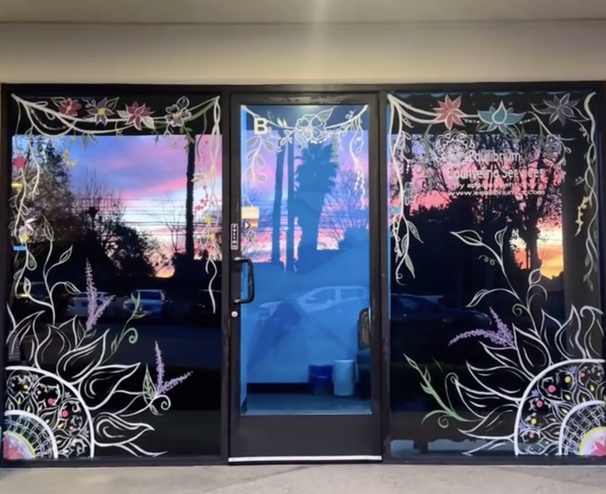 A storefront at sunset with florals, vines, and mandalas hand painted across the windows and door
