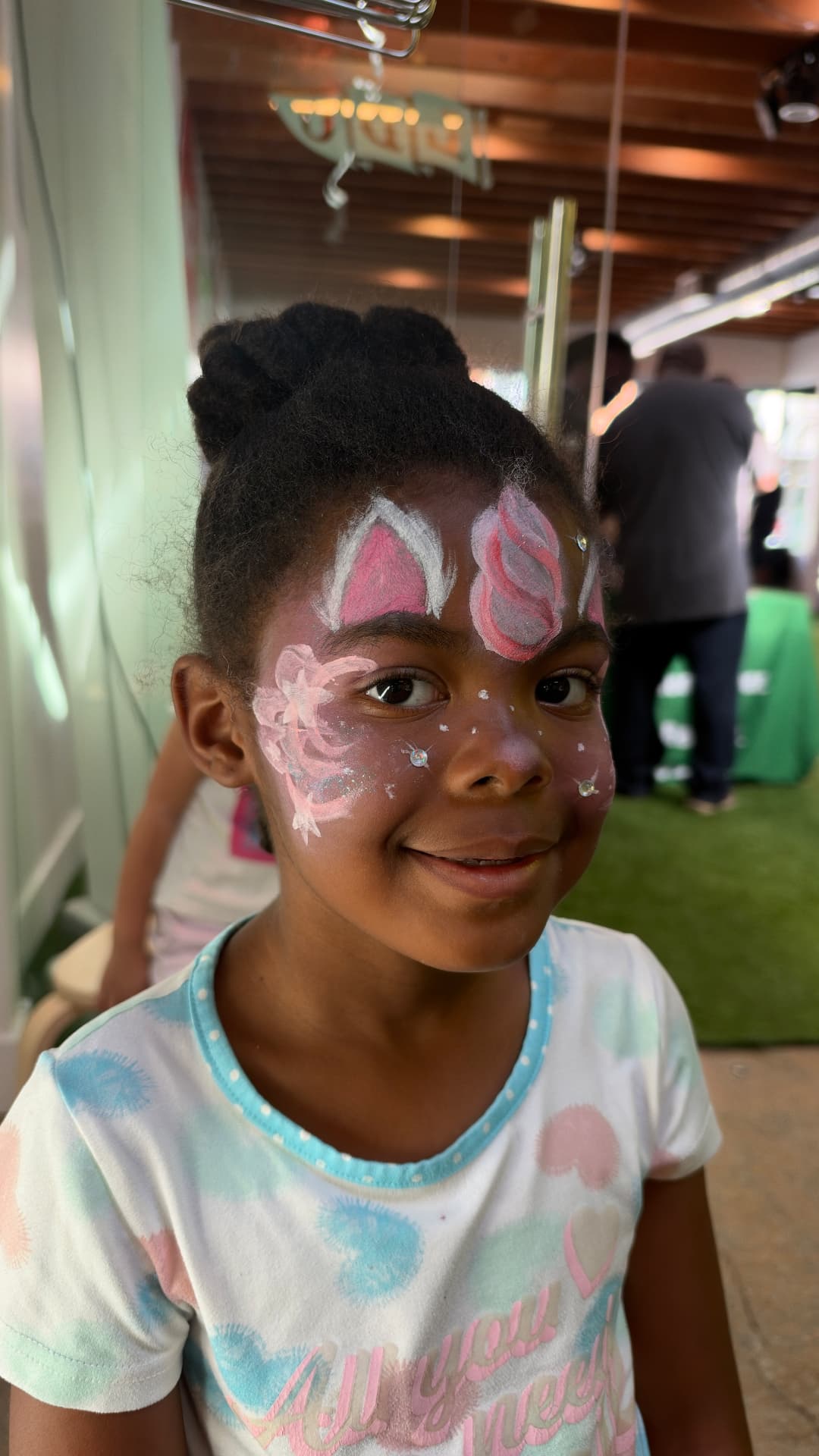 A smiling young guest with a pink unicorn face painting, glitter, and gems