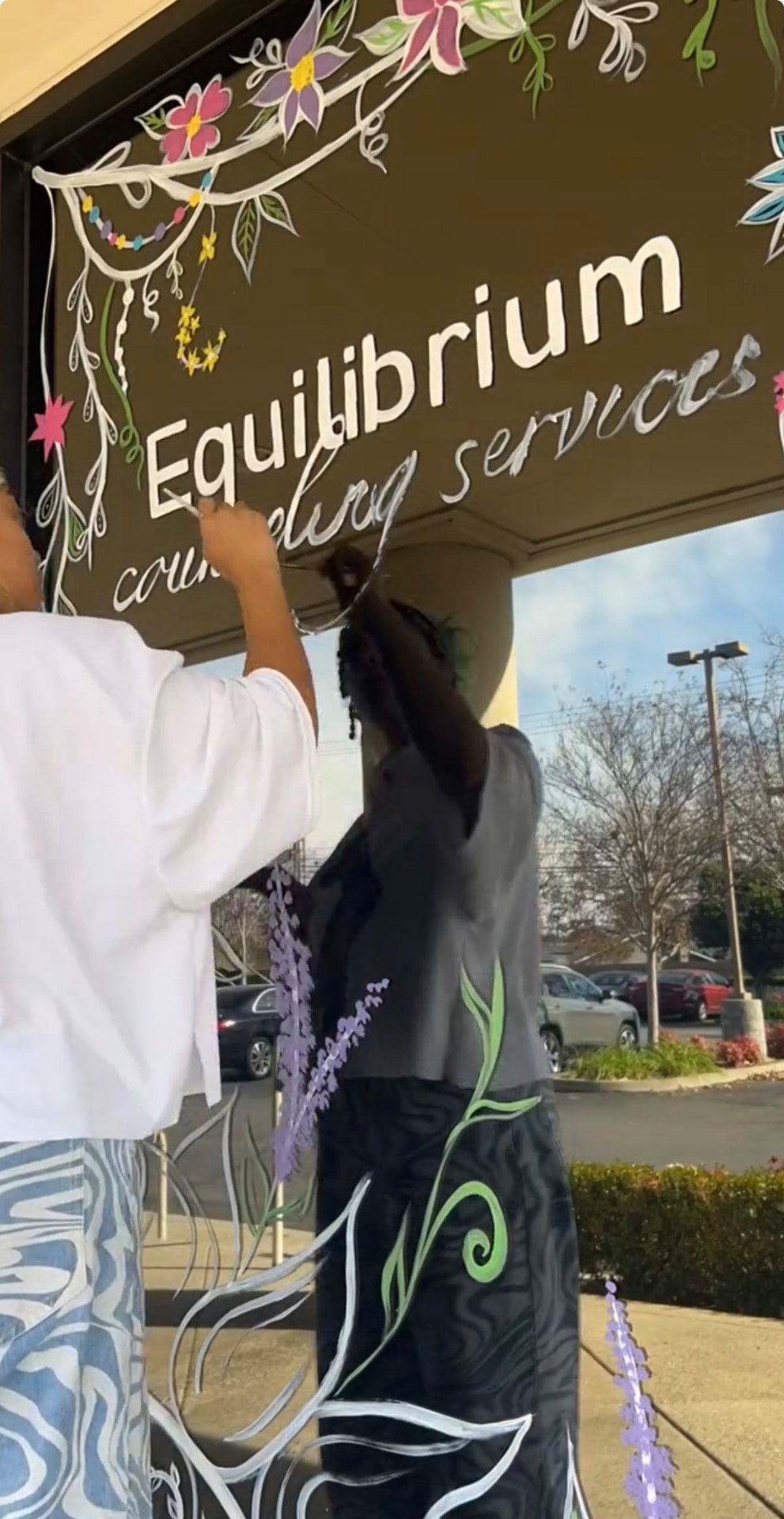 Hand lettering a business name onto glass surrounded by painted florals